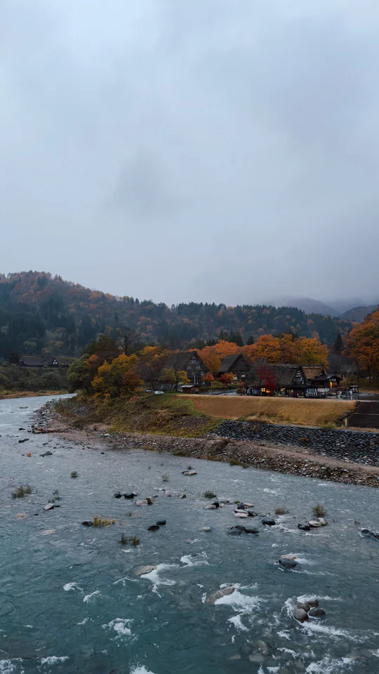 Picturesque view of Shirakawa-go village with autumn colors and a serene river.