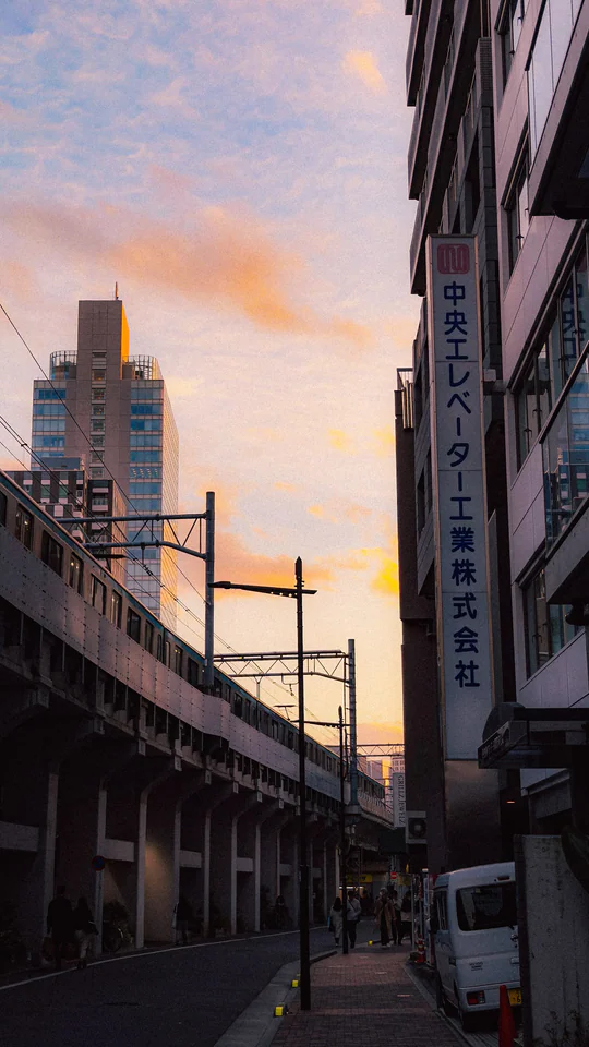Vibrant sunset over a Japanese city street with modern architecture and elevated railway.