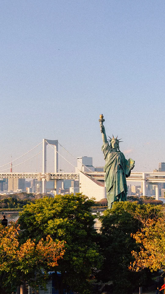 Statue of Liberty replica with Rainbow Bridge in Odaiba, Tokyo during daytime.