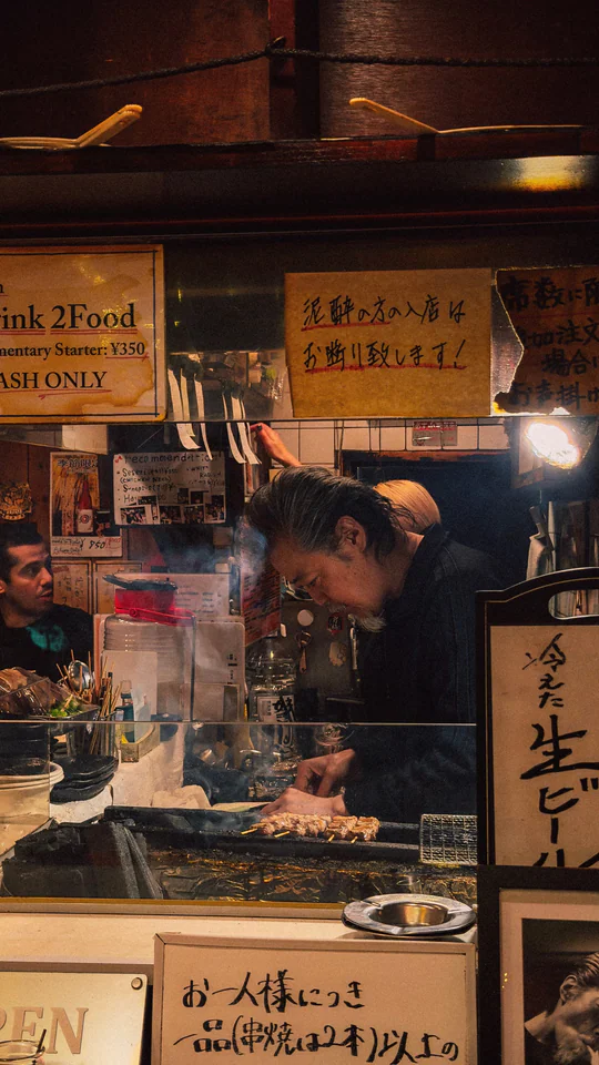 Chef preparing yakitori at traditional Japanese food stall at night.