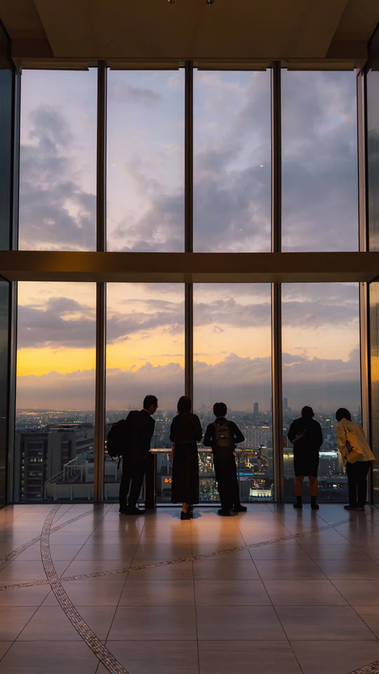 Silhouetted people enjoying the Tokyo skyline view at sunset through a large window.
