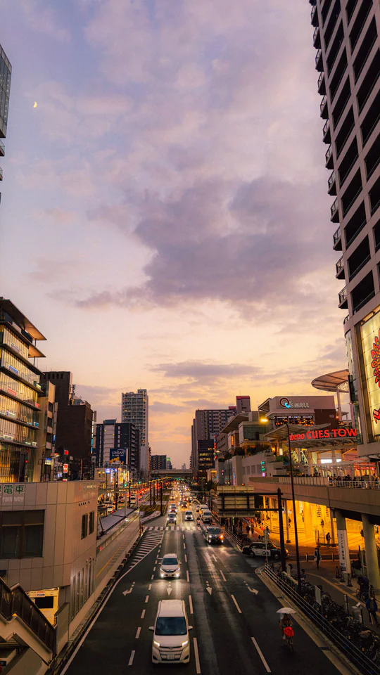 Urban evening scene in Japan with vibrant street life and towering buildings under a colorful sky.