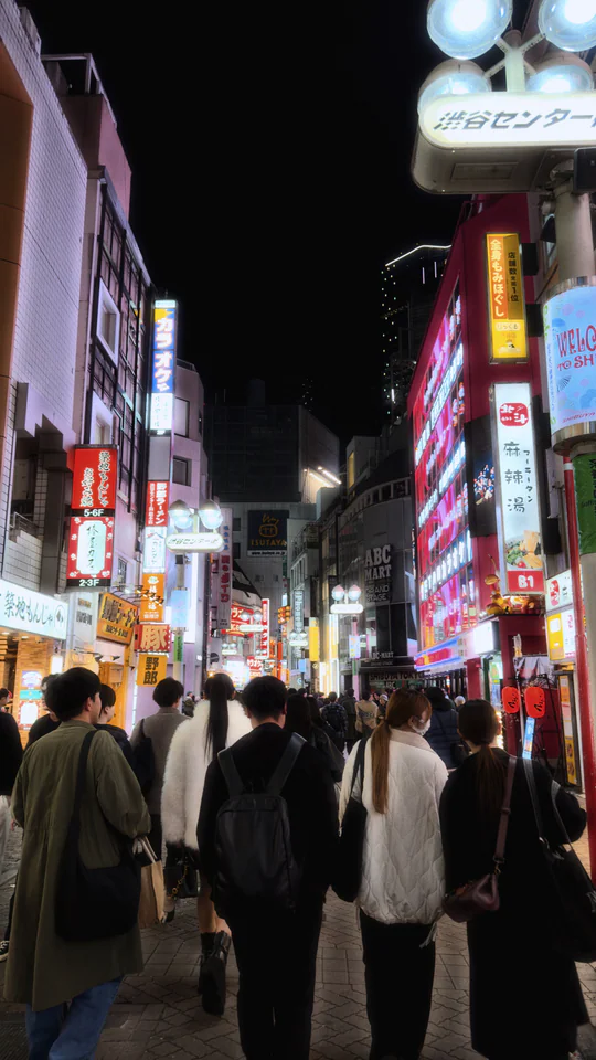 Bustling Shibuya street at night with neon lights and diverse crowd, capturing Tokyo's vibrant atmosphere.