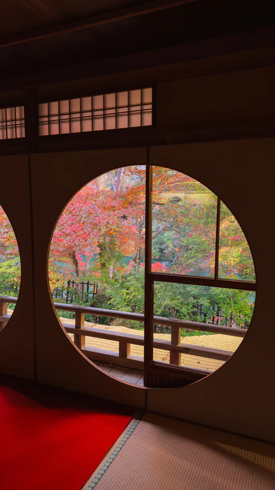 Circular window view of vibrant autumn foliage at a Japanese temple
