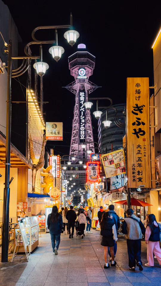 Bustling night scene at Tsutenkaku Tower in Osaka with illuminated streets and lively crowd.