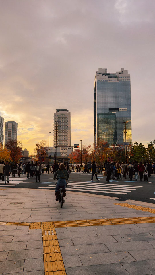Cyclist on a bustling Osaka street with Umeda Sky Building at sunset.