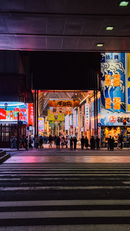 Night view of a lively Japanese shopping arcade illuminated with neon lights and bustling with people.
