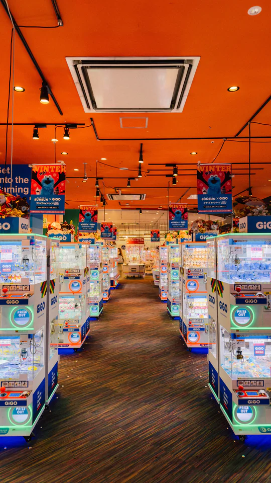 Bright arcade in Japan featuring rows of colorful claw machines under orange ceiling.